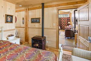 Bedroom with a wood stove, wood walls, and wooden ceiling