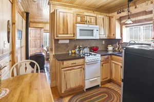 Kitchen with white appliances, backsplash, wood ceiling, plenty of natural light, and decorative light fixtures