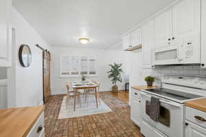 Kitchen with a barn door, white appliances, brick flooring, and white cabinets