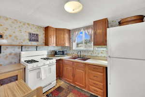 Kitchen featuring wallpapered walls, white appliances, wood finish cabinetry, and a textured ceiling