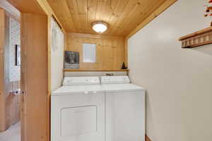 Laundry area with wood ceiling, separate washer and dryer, wood walls, and electric panel