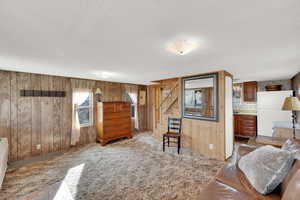 Living area featuring light colored carpet, a textured ceiling, and wooden walls