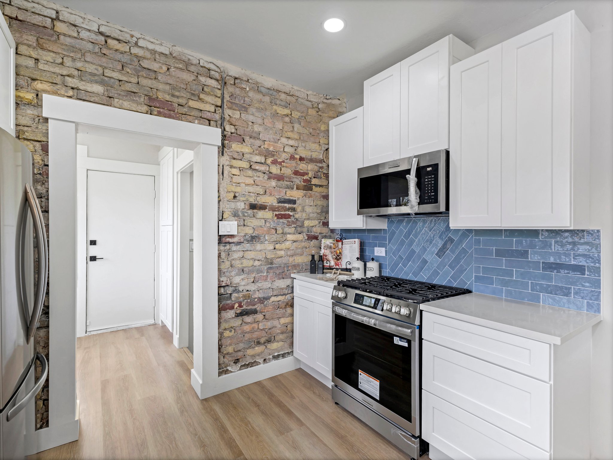 Kitchen featuring stainless steel appliances, white cabinetry, decorative backsplash, light wood-style flooring, and light stone counters