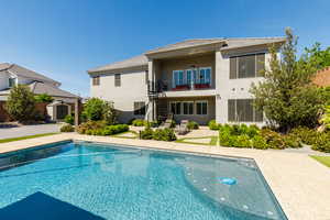 Rear view of property with a balcony, a patio, a storage shed, stucco siding, and an outdoor pool