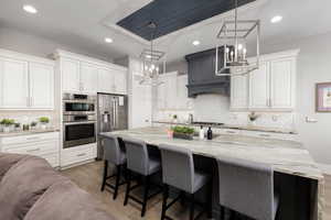 Kitchen with light stone countertops, a kitchen bar, stainless steel appliances, white cabinetry, and backsplash