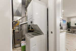 Laundry area featuring stacked washer / drying machine, heating unit, light wood-type flooring, and recessed lighting