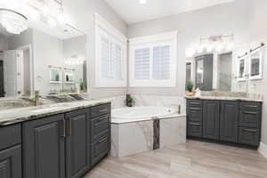 Full bath with two vanities, a bath, light wood finished floors, and hanging lights