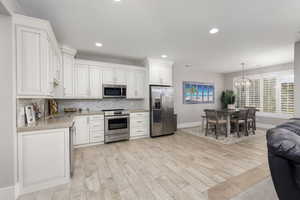 Kitchen with stainless steel appliances, light wood-style flooring, white cabinets, backsplash, and suspended lighting