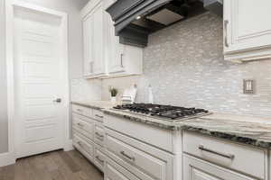 Kitchen with white cabinetry, light stone counters, dark wood finished floors, backsplash, and stainless steel gas stovetop