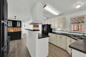 Kitchen with dark countertops, backsplash, a textured ceiling, light wood finished floors, and black fridge with ice dispenser