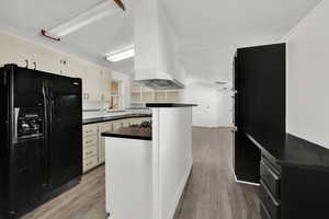 Kitchen featuring black fridge with ice dispenser, dark countertops, light wood-type flooring, a textured ceiling, and white cabinets