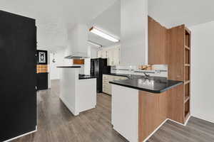 Kitchen featuring open shelves, a peninsula, dark countertops, and black fridge with ice dispenser