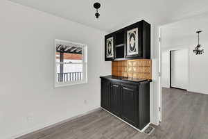 Kitchen featuring dark cabinetry, dark countertops, decorative backsplash, light wood-type flooring, and crown molding