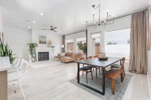 Dining area featuring light wood-style floors, a ceiling fan, a fireplace, and suspended lighting