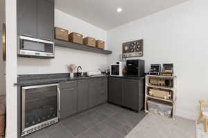 Bar area with dark countertops, beverage cooler, stainless steel microwave, dark tile patterned flooring, and open shelves