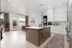Dual tone kitchen featuring modern cabinets, an island with sink, light stone counters, stainless steel appliances, and hanging light fixtures