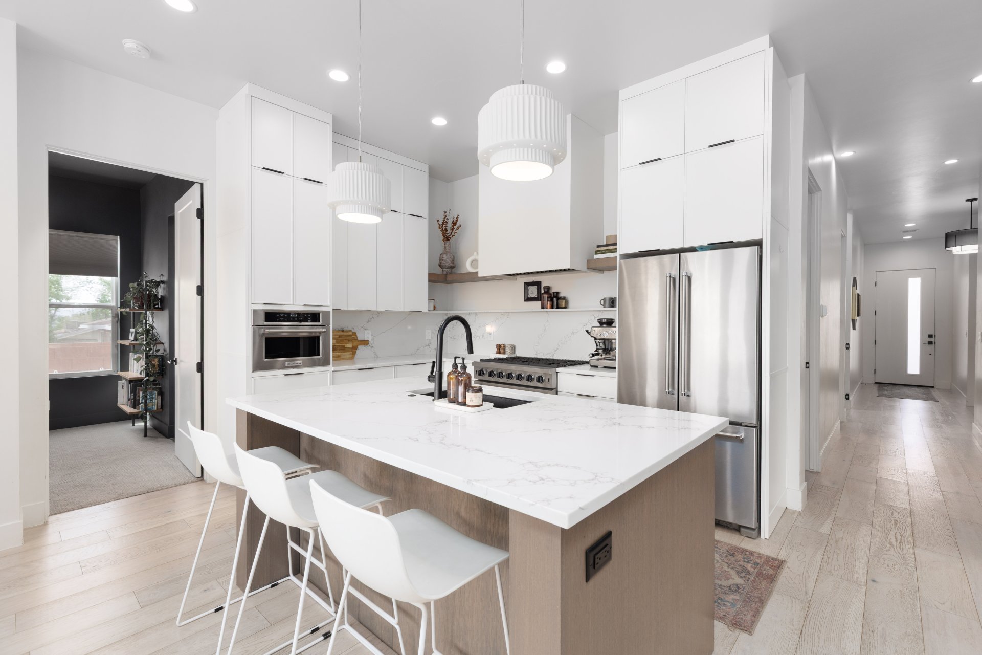 Kitchen with hanging light fixtures, premium appliances, light wood finished floors, light stone counters, and two tone cabinets