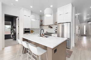 Kitchen with hanging light fixtures, premium appliances, light wood finished floors, light stone counters, and two tone cabinets