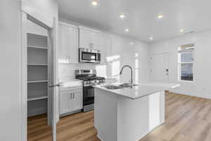 Kitchen with stainless steel appliances, a kitchen island with sink, white cabinetry, light wood-style floors, and recessed lighting