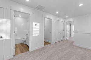 Unfurnished bedroom featuring ensuite bath, light colored carpet, a closet, and recessed lighting