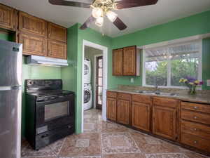 Kitchen with black range with electric stovetop, freestanding refrigerator, wood finish cabinets, a ceiling fan, and light countertops