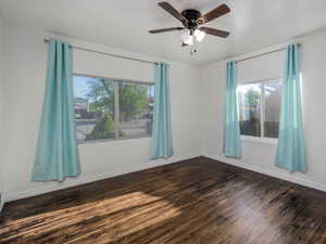 Unfurnished room with dark wood-style floors, ceiling fan, and plenty of natural light