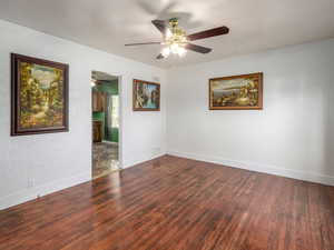 Empty room with dark wood finished floors, a ceiling fan, and a textured wall