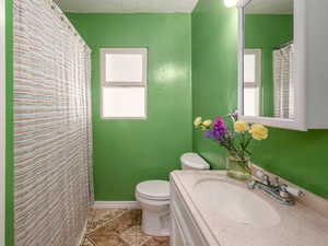 Full bath featuring curtained shower, vanity, plenty of natural light, a textured ceiling, and light tile patterned floors