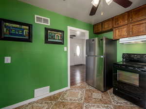 Kitchen with black range with electric stovetop, freestanding refrigerator, a ceiling fan, wood finish cabinetry, and water heater