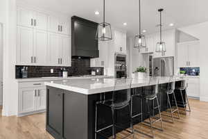 Two tone kitchen with decorative backsplash, a large island, two tone cabinets, stainless steel appliances, and light wood-style flooring