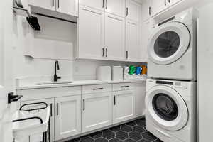 Laundry area featuring cabinet space, stacked washer and clothes dryer, and dark tile patterned floors