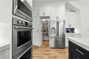 Kitchen with stainless steel appliances, light stone counters, two tone cabinetry, light wood-style flooring, and backsplash