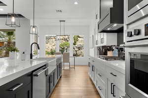 Two tone kitchen featuring dual tone cabinetry, stainless steel appliances, light stone countertops, light wood finished floors, and backsplash