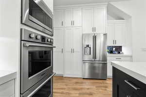 Kitchen with stainless steel appliances, light stone counters, two tone color scheme, and light wood-type flooring