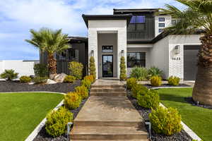 View of exterior entry with brick siding, a lawn, and stucco siding