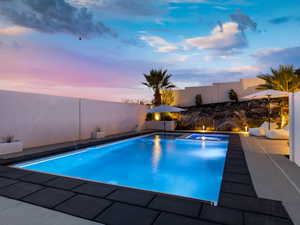 Pool at dusk with a fenced backyard, a patio area, and a pool with connected hot tub