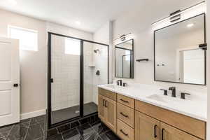Bathroom with a shower stall, double vanity, dark marble finish flooring, and recessed lighting