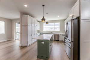 Two tone kitchen with two tone cabinetry, stainless steel appliances, light wood-style flooring, a center island, and light stone countertops