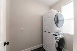 Laundry room with stacked washing machine and dryer and dark tile patterned flooring