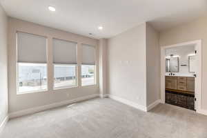 Unfurnished bedroom with light colored carpet, ensuite bathroom, and recessed lighting