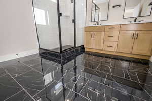 Bathroom featuring a stall shower, double vanity, and dark marble finish flooring