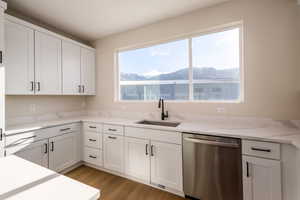 Kitchen featuring stainless steel dishwasher, white cabinetry, light wood-style floors, light stone countertops, and a mountain view