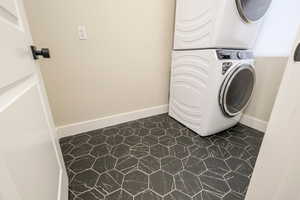 Laundry area featuring stacked washer / drying machine and dark tile patterned floors
