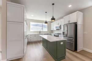 Two tone kitchen with two tone color scheme, stainless steel appliances, light wood-type flooring, light stone countertops, and a kitchen island