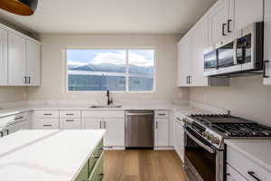 Kitchen with stainless steel appliances, light stone counters, healthy amount of natural light, and two tone cabinetry
