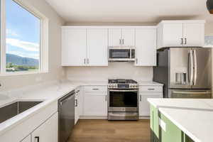 Two tone kitchen with stainless steel appliances, light stone countertops, light wood finished floors, a mountain view, and two tone color scheme
