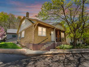 Bungalow-style house featuring brick siding, a chimney, and covered porch
