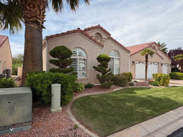 Mediterranean / spanish home with a tile roof, stucco siding, a garage, and a front lawn