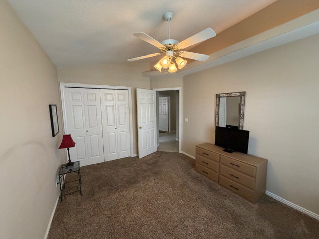 Unfurnished bedroom with dark colored carpet, a closet, ceiling fan, and lofted ceiling