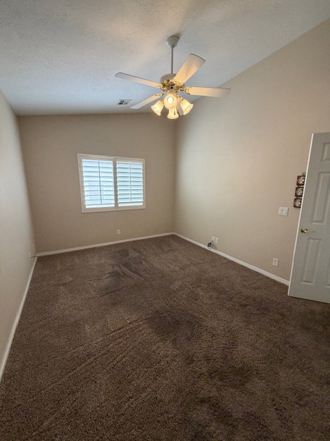 Unfurnished room with vaulted ceiling, dark colored carpet, and ceiling fan
